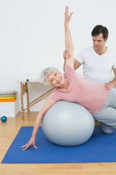 Physical therapist assisting senior woman with yoga ball in the gym at hospital