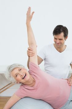 Physical therapist assisting senior woman with yoga ball in the gym at hospital