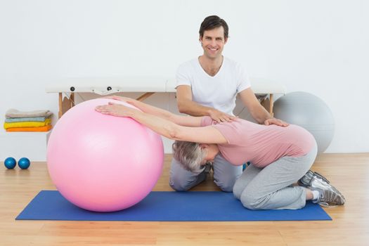Portrait of a physical therapist assisting senior woman with yoga ball in the gym at hospital