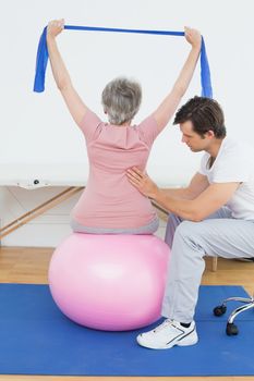 Senior woman sitting on yoga ball while working with a physical therapist