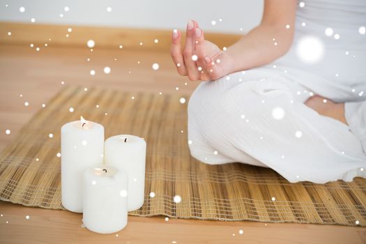Woman sitting in lotus pose beside white candles against snow