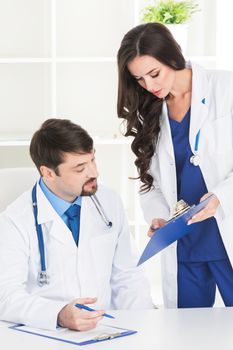 Professional medical doctor and his assistant working in the office, she is holding a clipboard and he is signing medical records