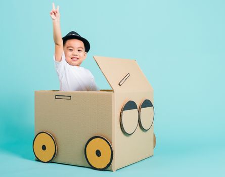 Happy Asian children boy smile in driving play car creative by a cardboard box imagination, summer holiday travel concept, studio shot on blue background with copy space for text