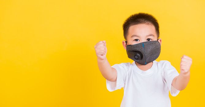 Asian Thai happy portrait cute little cheerful child boy wearing mask protective for covid-19 or pm2.5 dust he raise hands glad excited cheerful after recovering from illness, on yellow background