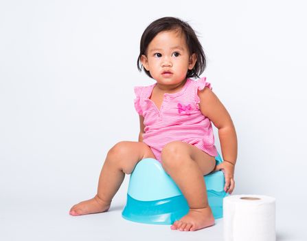 Asian little cute baby child girl education training to sitting on blue chamber pot or potty with toilet paper rolls, studio shot isolated on white background, wc toilet concept