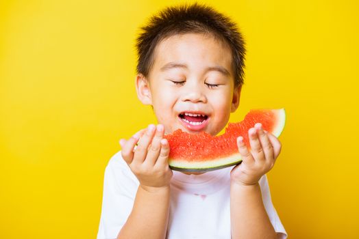 Happy portrait Asian child or kid cute little boy attractive laugh smile playing holds cut watermelon fresh for eating, studio shot isolated on yellow background, healthy food and summer concept