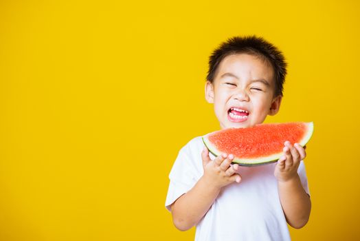 Happy portrait Asian child or kid cute little boy attractive laugh smile playing holds cut watermelon fresh for eating, studio shot isolated on yellow background, healthy food and summer concept