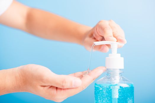 Close up Asian young woman applying press dispenser sanitizer alcohol gel pump to hand wash cleaning, hygiene prevention COVID-19 or coronavirus protection concept, isolated on blue background