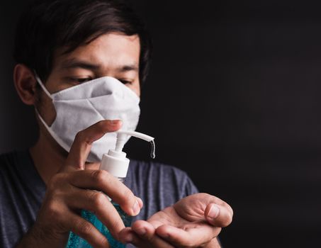 Closeup Asian handsome man wearing protective face mask fear in eye holding show sanitizer gel near face, hygiene prevention COVID-19 virus or coronavirus protection concept dark on black background