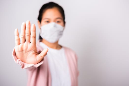 Asian woman wearing surgical protection face mask hygiene against coronavirus her raising hand stop sign, studio shot isolated on white background with copy space, COVID-19 or corona virus concept