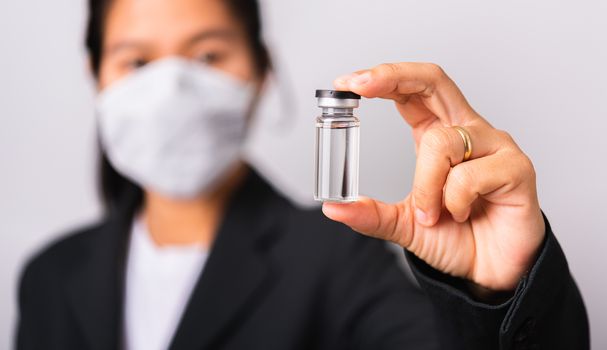 Asian woman doctor wearing surgical protective cloth face mask against coronavirus her hold ampoule bottle vaccine focus on  glass transparent, studio shot isolated white background, COVID-19 concept