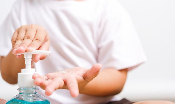 Closeup Asian little child boy sitting applying bottle pump dispenser sanitizer alcohol gel cleaning washing hands yourself, COVID-19 or coronavirus protection concept, isolated on white background with copy space