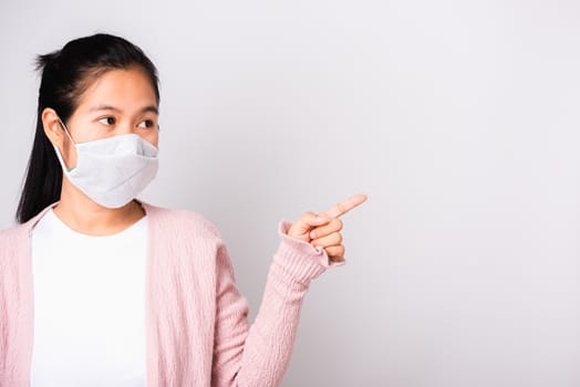 Asian beautiful woman wearing surgical protection face mask hygiene against coronavirus her pointing to side, studio shot isolated on white background with copy space, COVID-19 or corona virus concept