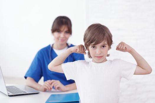 Healthy child showing muscles at pediatrician office female doctor on background