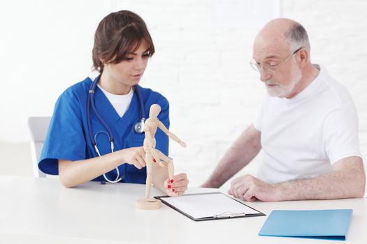 Doctor talking to senior man about joint disease using wooden doll
