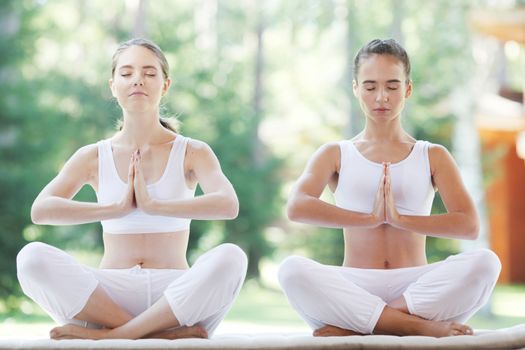 Women in white sportswear sitting in lotus position during group yoga training at park