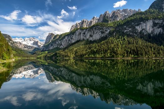 Panoramic view of idyllic summer landscape in the Alps with clear mountain lake and fresh green mountain pastures in the background