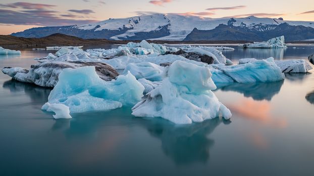 Little red sailboat cruising among floating icebergs in Disko Bay glacier during midnight sun season of polar summer. Ilulissat, Greenland.