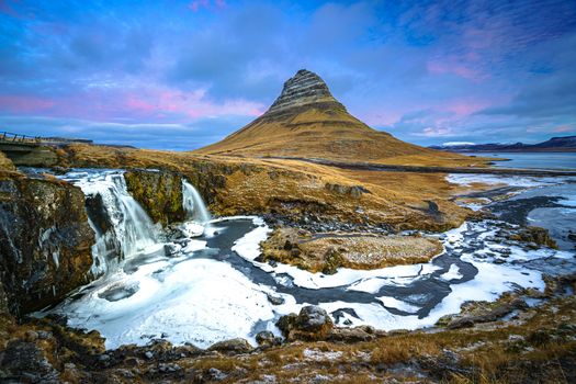 Colorful Icelandic landscapes under gray heavy sky. Green wet grass, beautiful lake, and snowy tops of the mountais reflected in the lake water.