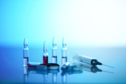 Syringe, ampoules and pills on glowing blue reanimation light background