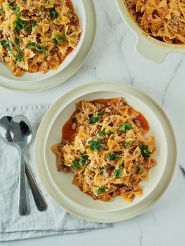 Pasta Farfalle with tomato sauce and ground meat in plate on white marble tabletop. Idea and recipes for easy, simple lunch or dinner one-pot meat goulash. Top down view or flat lay. Vertical