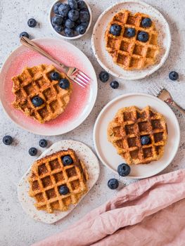 Easy healthy gluten free oat waffles with copy space. Plates with appetizing homemade waffles with oat flour decorated blueberries, on light gray cement background. Vertical. Top down view or flat lay