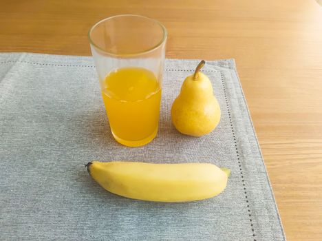 Banana, pear and glass of orange juice, on fabric towel, on the table and blurred background.