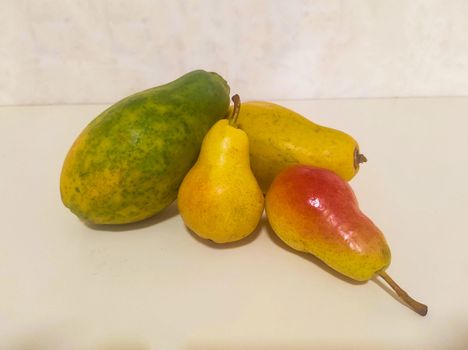 Close up of papaya and pear on light background. Whole ripe yellow fruits.