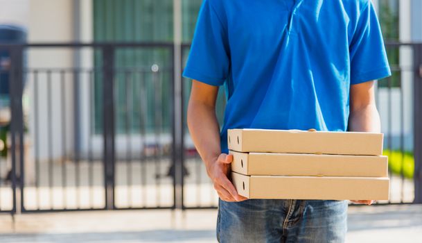 Asian Young delivery man courier online with food order is pizza boxes in uniform he protective face mask, service customer in front of the house under curfew quarantine pandemic coronavirus COVID-19