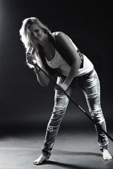 young, girl, blonde, jeans, clothes on a dark background emotionally sings into a microphone