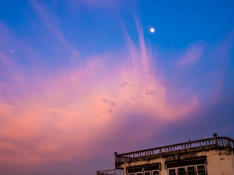 Pink clouds and moon in sunset sky and the old building