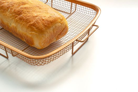 An isolated homemade white bread on a cooling rack on white table