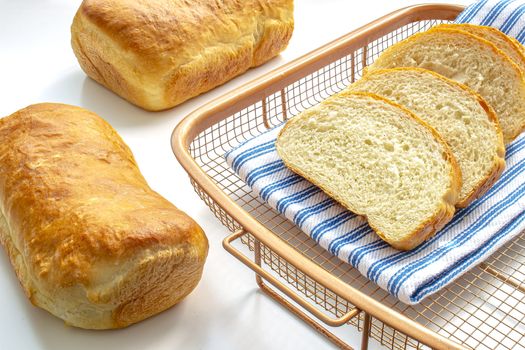 A couple of homemade white bread on a cooling rack with a cloth on white table