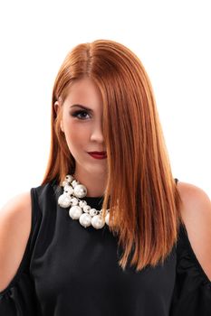 Head shot of a beautiful redheaded young woman with clean make up, stylish black blouse and modern necklace, hair covering half of her face, isolated on white background. Fashion and beauty concept.