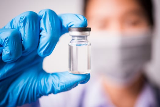 Closeup hand of woman doctor or scientist in doctor's uniform wearing face mask protective in lab holding medicine liquid vaccines vial bottle, coronavirus or COVID-19 concept, studio shot isolated
