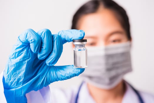 Closeup hand of woman doctor or scientist in doctor's uniform wearing face mask protective in lab holding medicine liquid vaccines vial bottle, coronavirus or COVID-19 concept, studio shot isolated