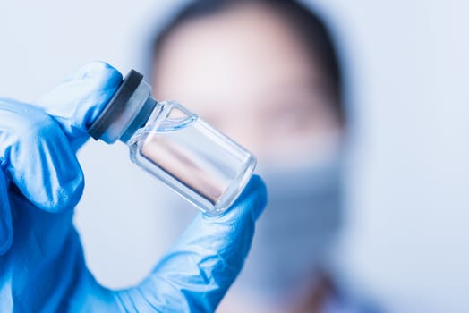 Closeup hand of woman doctor or scientist in doctor's uniform wearing face mask protective in lab holding medicine liquid vaccines vial bottle, coronavirus or COVID-19 concept, studio shot isolated