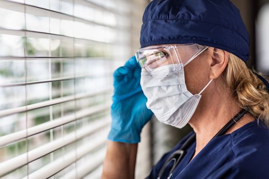 Female Doctor or Nurse On Break At Window Wearing Medical Face Mask and Goggles.