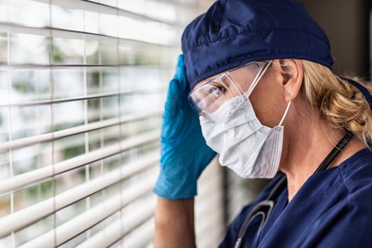 Female Doctor or Nurse On Break At Window Wearing Medical Face Mask and Goggles.