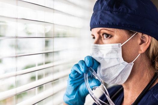 Female Doctor or Nurse On Break At Window Wearing Medical Face Mask and Goggles.