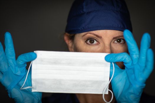 Female Doctor or Nurse Wearing Surgical Gloves Holding Up Medical Face Mask.