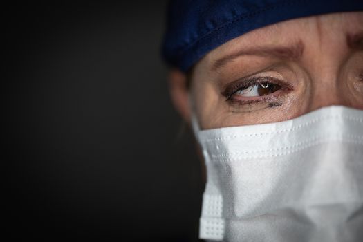 Tearful Stressed Female Doctor or Nurse Wearing Medical Face Mask on Dark Background.