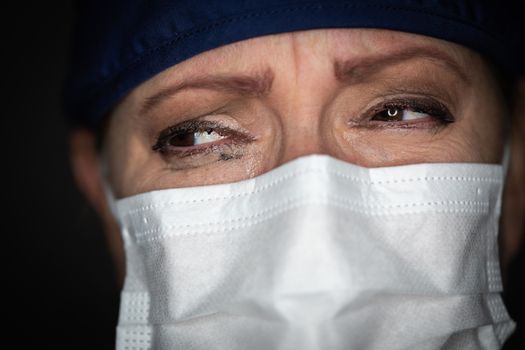 Tearful Stressed Female Doctor or Nurse Wearing Medical Face Mask on Dark Background.