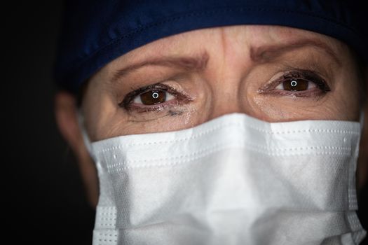 Tearful Stressed Female Doctor or Nurse Wearing Medical Face Mask on Dark Background.