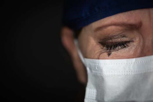 Tearful Stressed Female Doctor or Nurse Wearing Medical Face Mask on Dark Background.