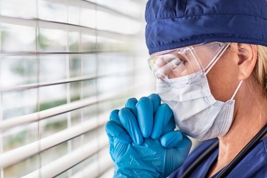 Stressed Female Doctor or Nurse On Break At Window Wearing Medical Face Mask and Goggles.
