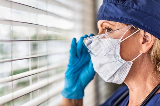 Female Doctor or Nurse On Break At Window Wearing Medical Face Mask and Goggles.