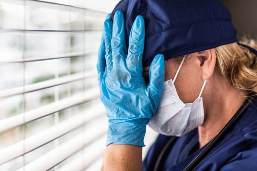 Stressed Female Doctor or Nurse On Break At Window Wearing Medical Face Mask and Goggles.