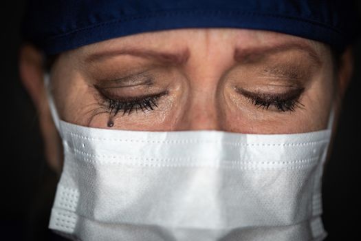 Tearful Stressed Female Doctor or Nurse Wearing Medical Face Mask on Dark Background.