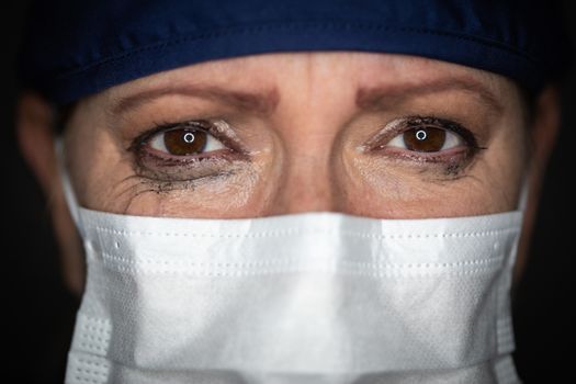 Tearful Stressed Female Doctor or Nurse Wearing Medical Face Mask on Dark Background.